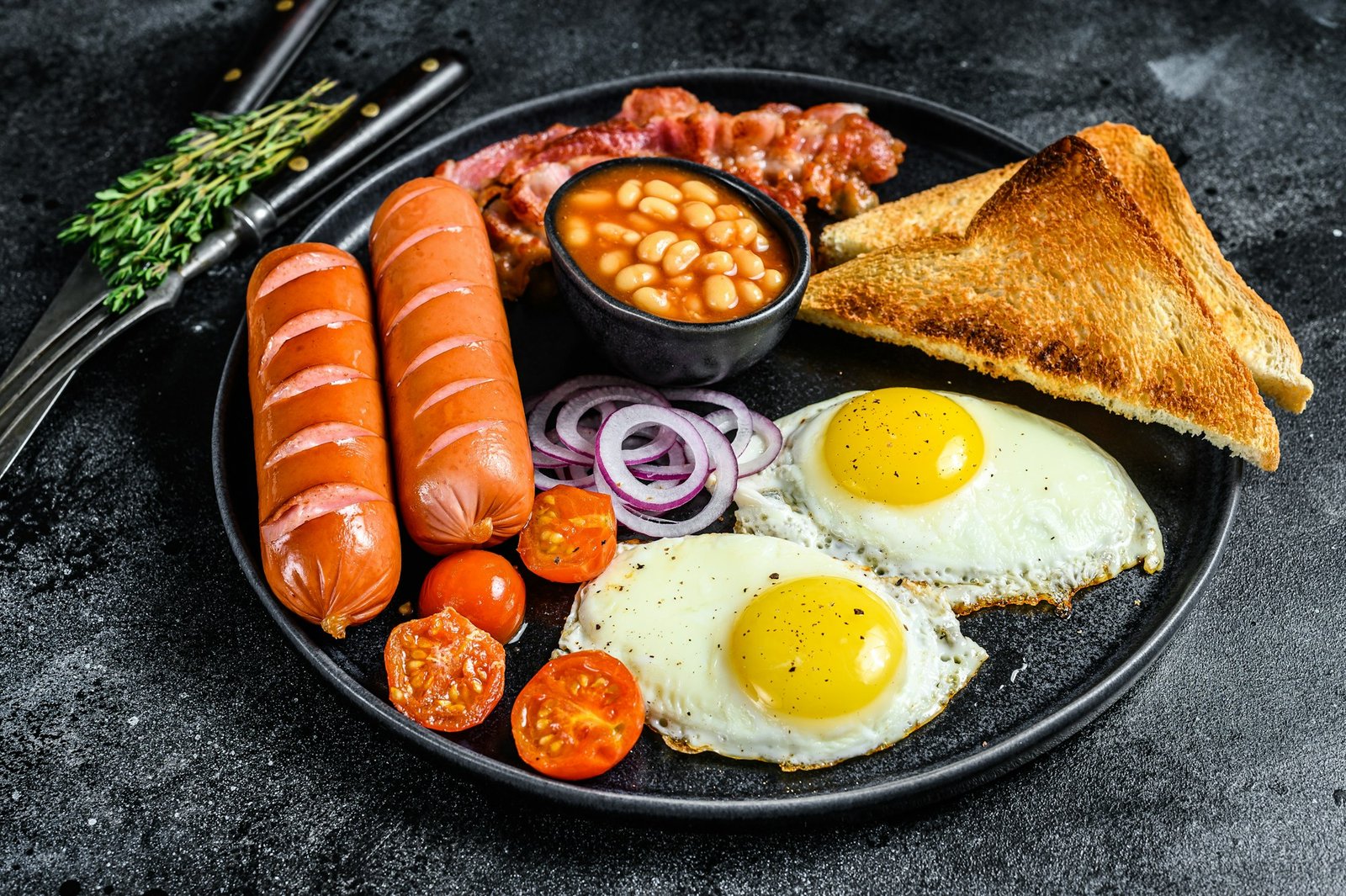 english breakfast with fried eggs, sausages, bacon, beans and toasts in a plate. Najhoršia možná ingrediencia na raňajky. Odborník na výživu vám radí, aby ste ju vyhodili z taniera