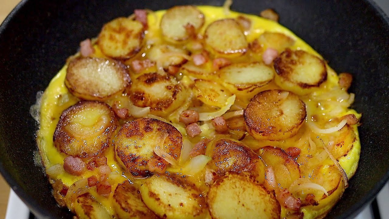 Einfach und lecker! Kartoffeln mit Zwiebeln, Speck und Eiern in einer Bratpfanne.